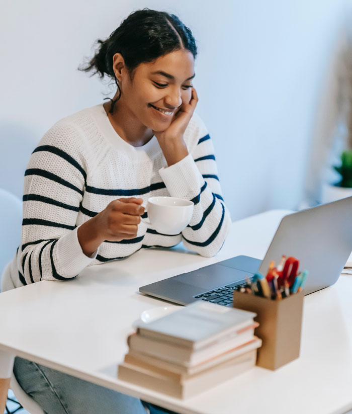 Smiling woman enjoying a coffee at home, browsing on a laptop to find fun things to do and avoid boredom.