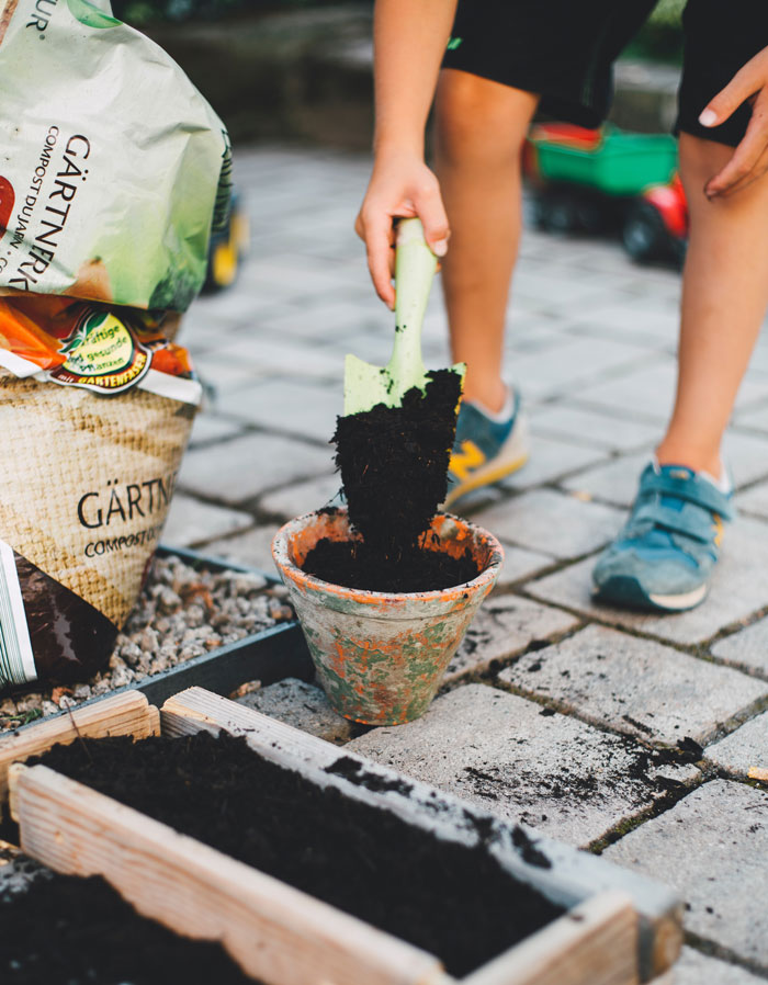 Person gardening at home, filling a pot with soil using a trowel, enjoying outdoor activities to avoid boredom.