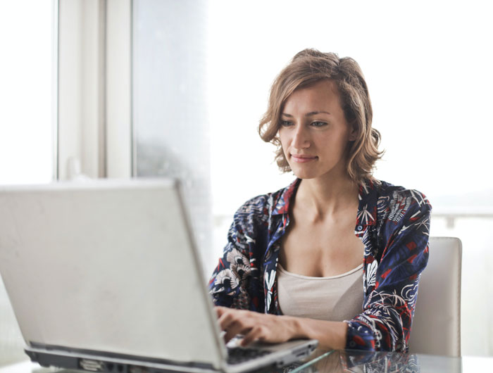 A woman in a patterned shirt uses a laptop at home for fun indoor activities.