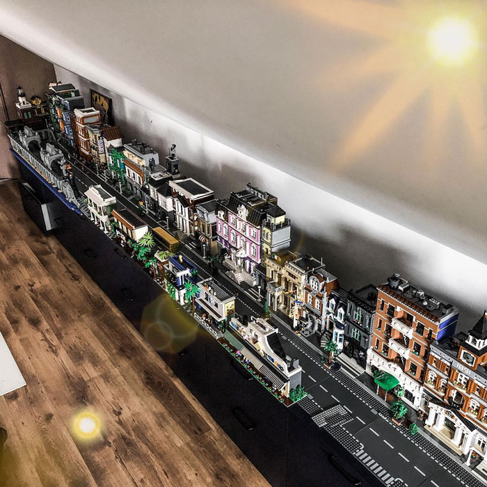 Detailed LEGO builds of a city street with buildings, trees, vehicles, and a boat on a long display table.