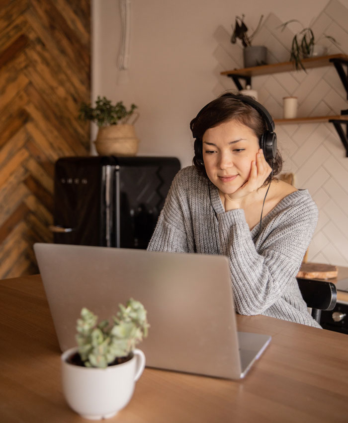 Person wearing headphones, using a laptop at home, enjoying fun activities to avoid boredom, with a plant in the foreground.