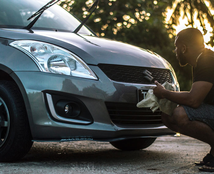 Man washing a car with a cloth, focusing on the front grille in sunlight, enjoying a fun activity to avoid boredom at home.