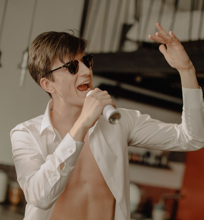 Person singing at home with a can as a microphone, dressed in sunglasses and an open shirt.