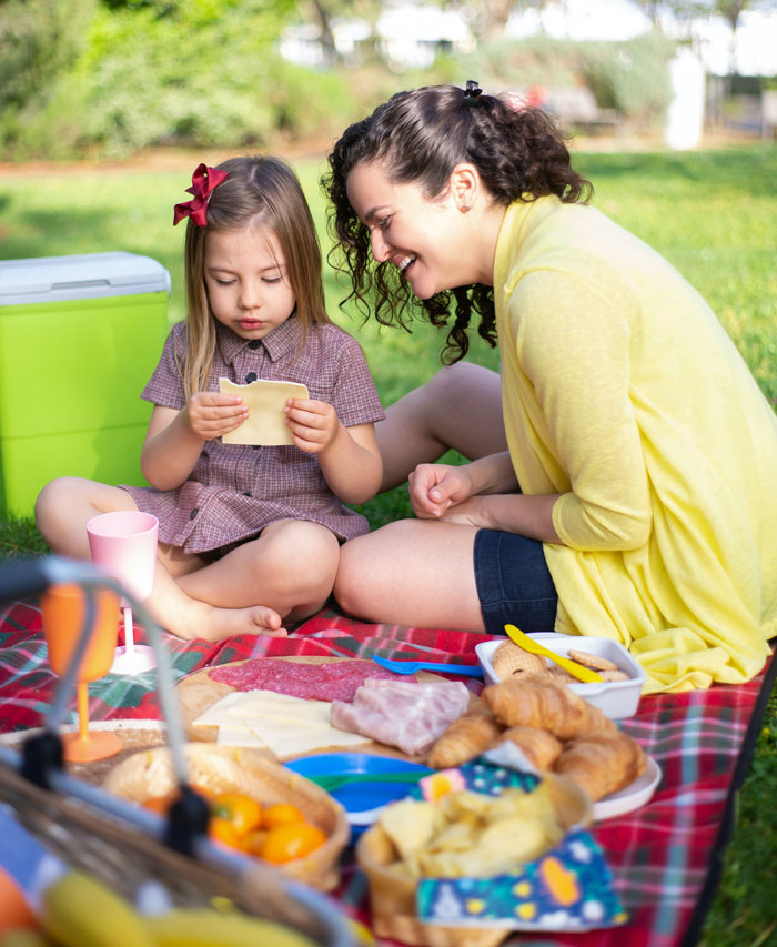 Child and woman enjoying a picnic on a blanket, surrounded by food, as a fun thing to do at home for avoiding boredom.