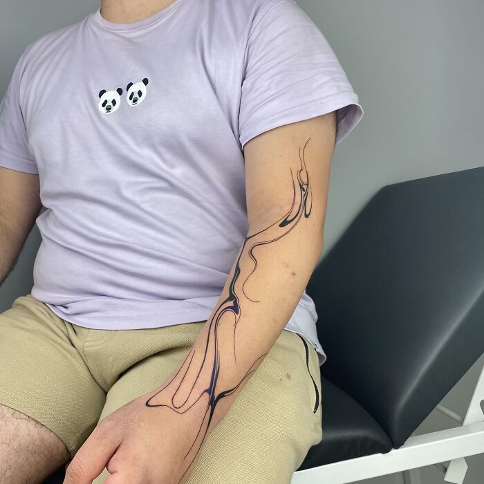 Man with a flowing tattoo design inspired by Sernakkab marbling on his arm, wearing a panda shirt and beige shorts. Man with a flowing tattoo design inspired by Sernakkab marbling on his arm, wearing a panda shirt and beige shorts.