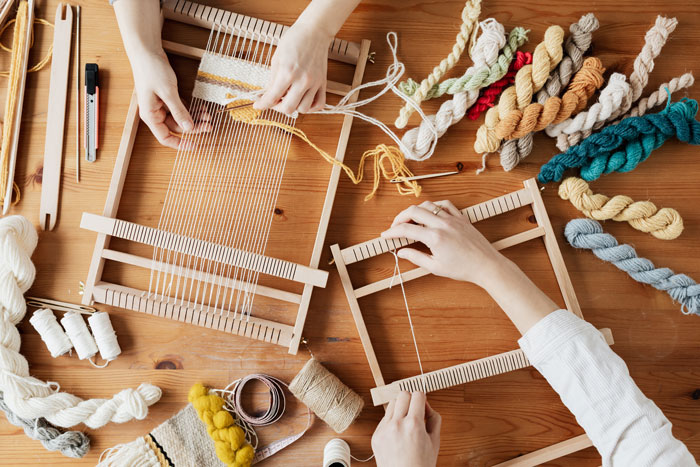 Hands weaving on wooden looms with colorful yarn, creating crafts to do at home and avoid boredom.