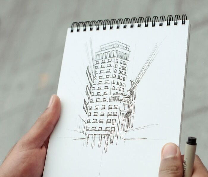 A hand holding a sketchpad with a detailed building drawing, perfect for drawing prompts inspiration.