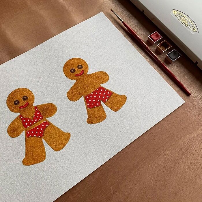 Two gingerbread figures in swimsuits painted on paper, with a paintbrush and watercolor set nearby.