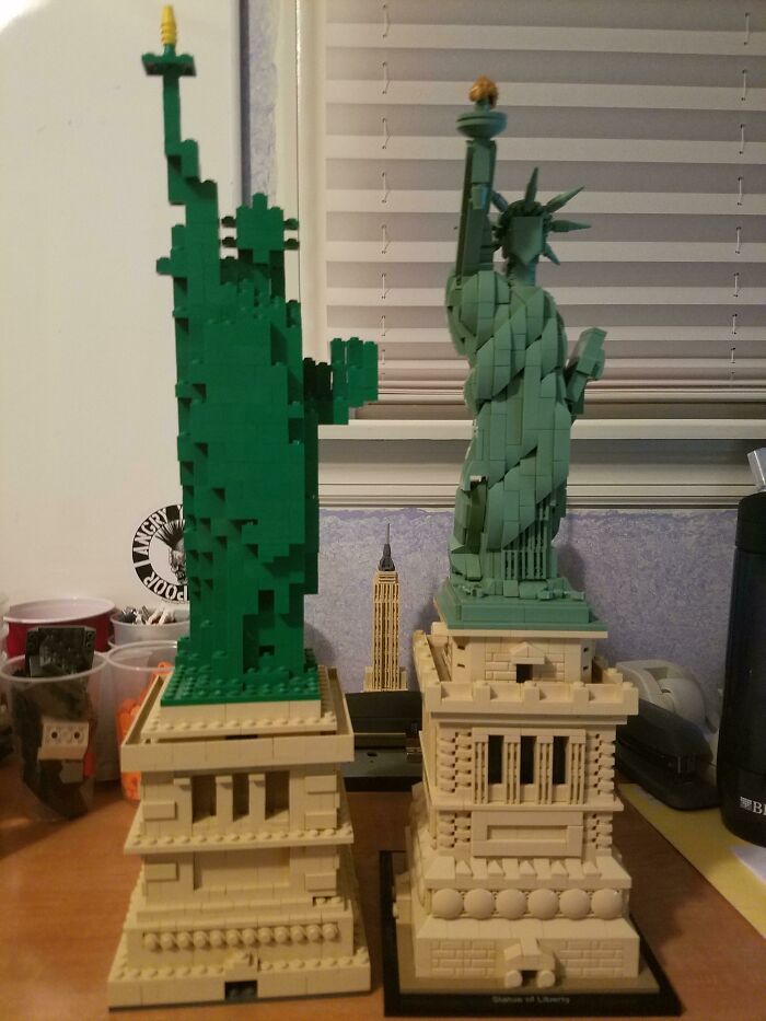 Two detailed LEGO builds of the Statue of Liberty displayed side by side on a desk with various items around.