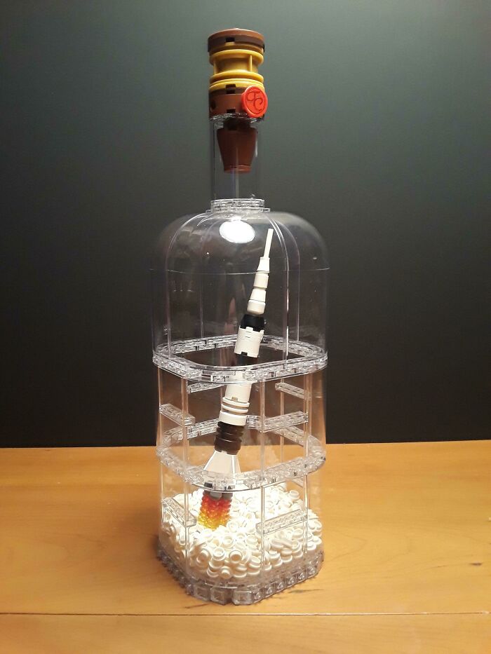 Clear LEGO build of a rocket inside a transparent bottle with detailed flames and intricate brick construction on a wooden surface.