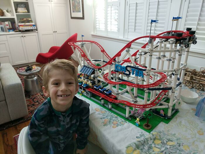 Young boy smiling next to a detailed LEGO roller coaster build showcasing incredible LEGO creations as works of art.