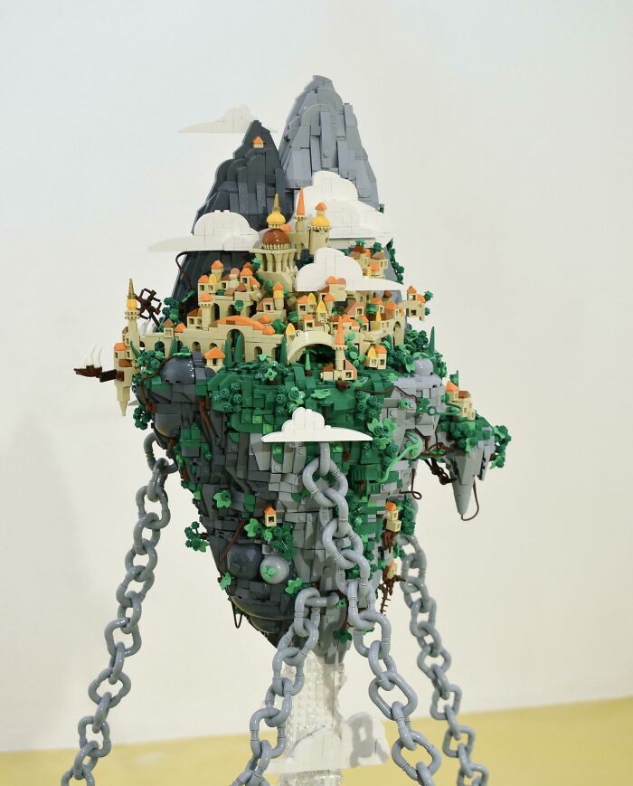 Intricate LEGO build of a floating island city with detailed buildings, greenery, and large chains anchoring it in place.