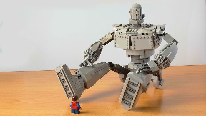 Incredible LEGO build of a large robot interacting with a small LEGO figure on a wooden surface.