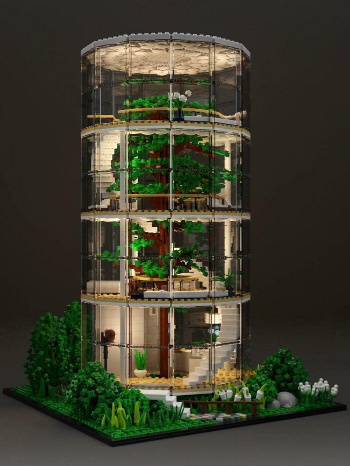 Intricate LEGO build of a modern glass building with a large tree inside and surrounding greenery, showcasing artful design.