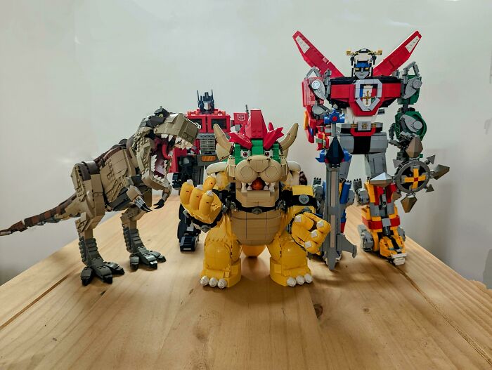 LEGO builds showcasing a dinosaur, robot, and characters in detailed and creative designs on a wooden surface.