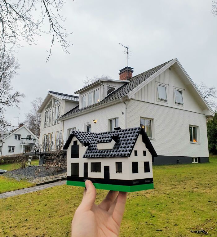 Hand holding a detailed LEGO house build in front of a real house, showcasing incredible LEGO builds as works of art.