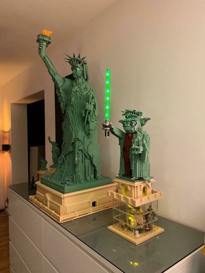 LEGO builds of the Statue of Liberty and Yoda holding a glowing green lightsaber displayed on a glass surface.