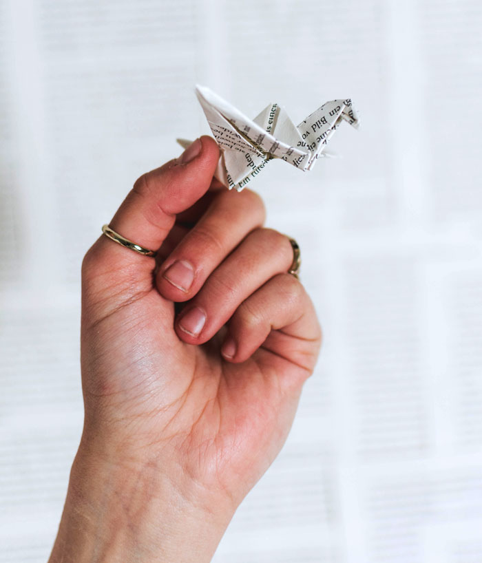 A hand holding a paper origami bird, showcasing a fun thing to do at home, avoiding boredom through creative crafting.