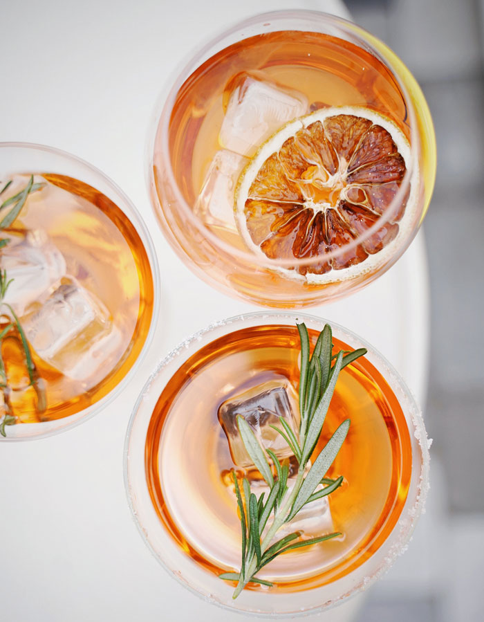 Three cocktails with ice, garnished with rosemary and dried citrus, capturing an enjoyable activity at home.