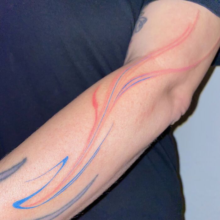 Arm with flowing tattoo design in red and blue, inspired by traditional marbling techniques. Arm with flowing tattoo design in red and blue, inspired by traditional marbling techniques.