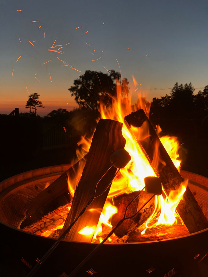 Roasting marshmallows over a home bonfire at sunset, sparks flying in the air.