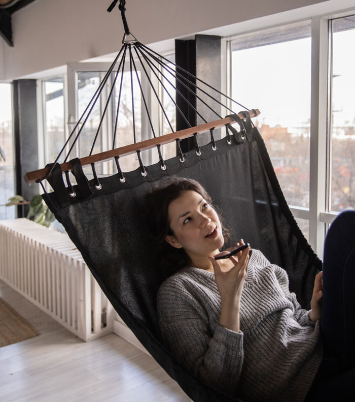 Woman relaxing in a hammock at home, talking on the phone, enjoying fun indoor leisure activities.