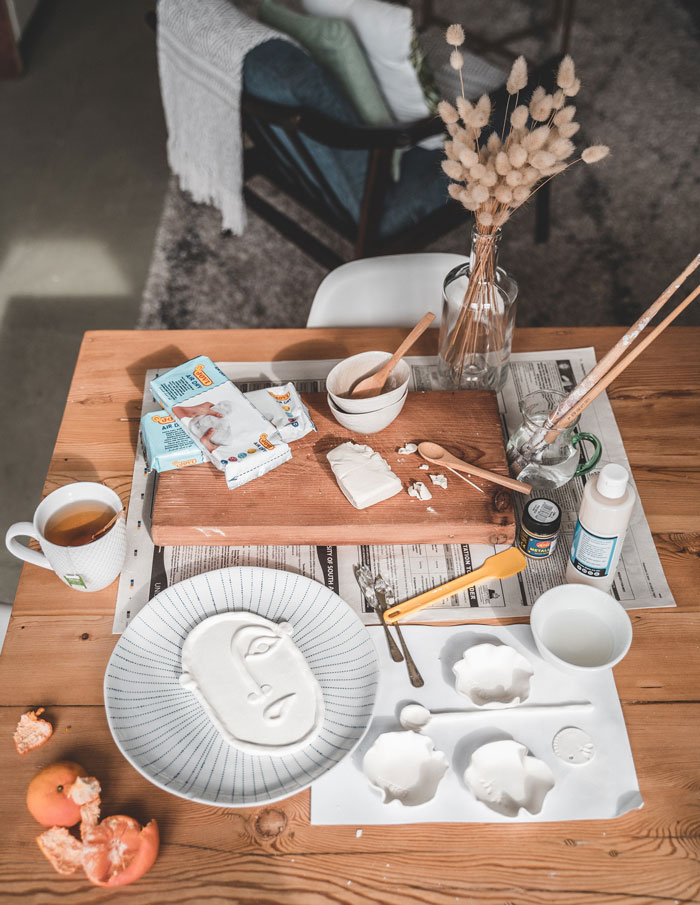 Crafting DIY face mask at home with clay and tools on a wooden table for a fun activity.