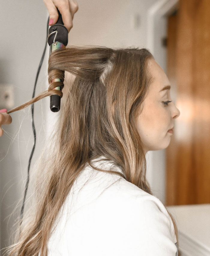 Person curling hair at home, using a curling iron, enjoying a fun activity to avoid boredom.