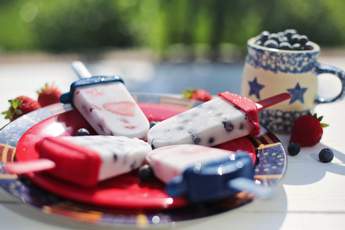Homemade fruit popsicles on a decorative plate, surrounded by strawberries and blueberries, perfect for fun activities at home.