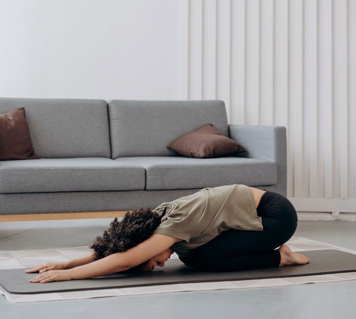 Person doing yoga at home to avoid boredom, stretching on a mat in front of a sofa.