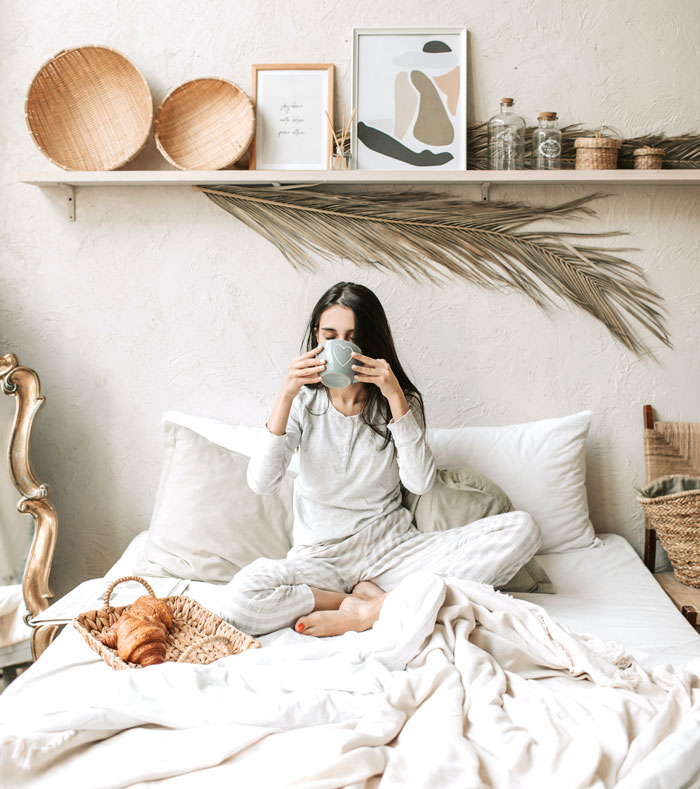 Woman enjoying coffee in bed with pastries, illustrating fun things to do at home.