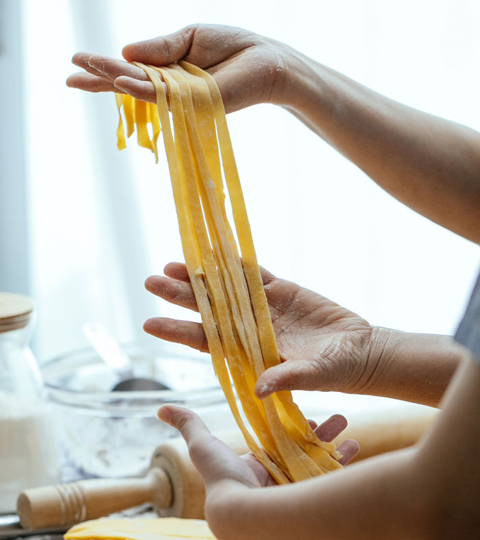 Hands holding freshly made pasta at home, showcasing a fun activity to avoid boredom.