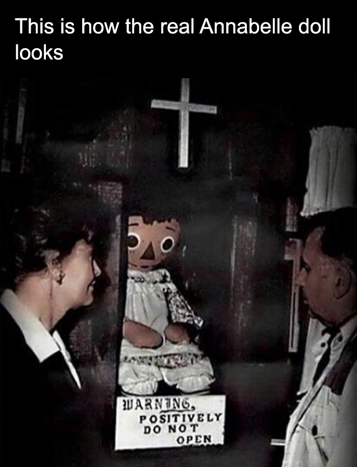 Real Annabelle doll displayed in a case with warning sign, viewed by two people, part of creepy facts and pictures collection.