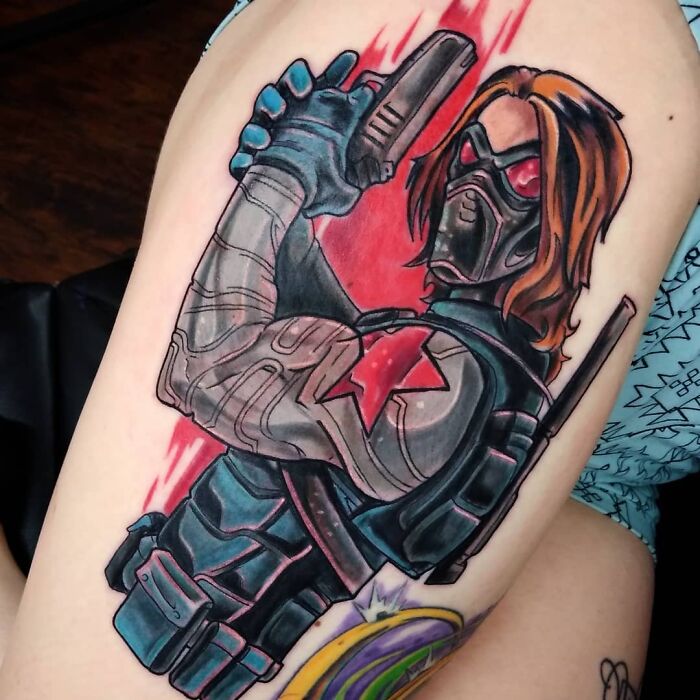 Marvel tattoo of masked character Bucky Barnes with a gun and long hair on a person's arm.