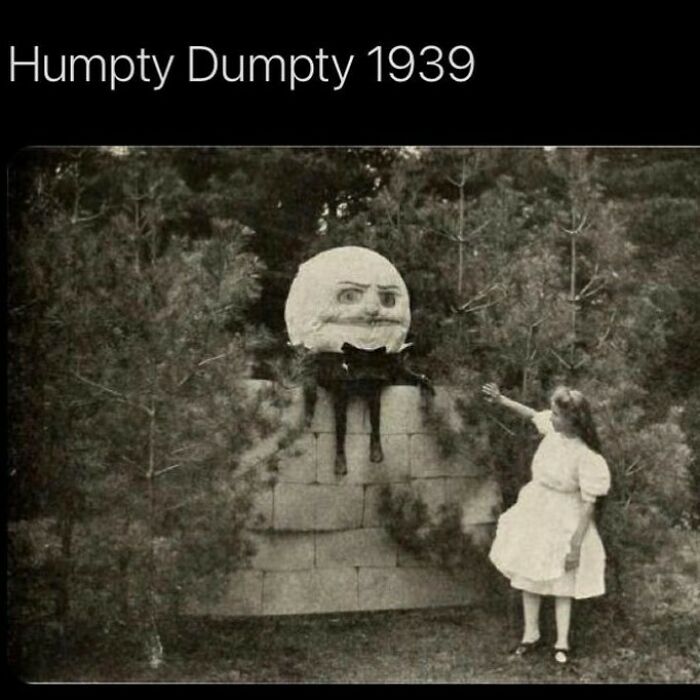 Creepy Humpty Dumpty figure from 1939 with eerie face and black cat, viewed by a girl in a vintage garden setting.