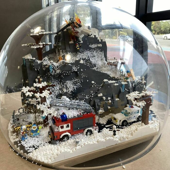 Detailed LEGO builds inside a clear dome featuring a snowy mountain scene with vehicles and a dragon sculpture.