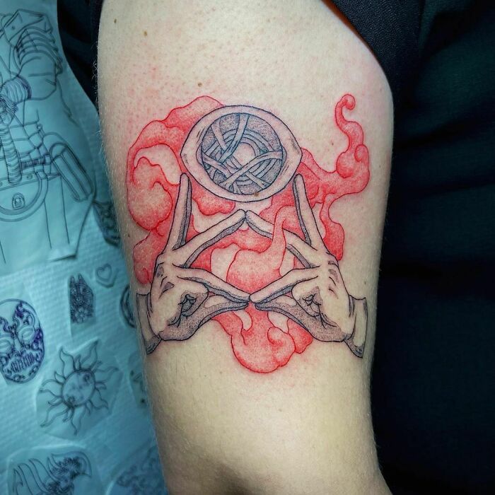 Marvel tattoo of hands creating a mystical symbol with red smoke on an arm.