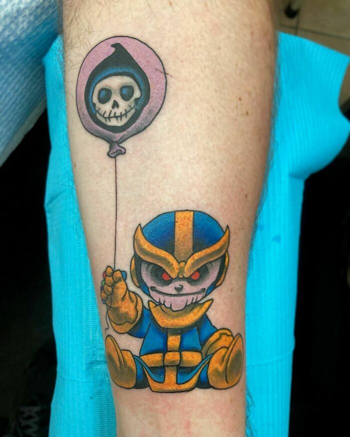 Marvel tattoo of a cartoon Thanos with a skull balloon on forearm.