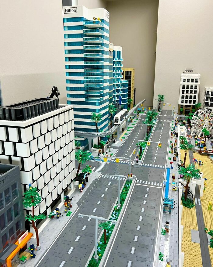 Intricate LEGO cityscape featuring tall buildings, roads, palm trees, and a beachfront Ferris wheel in a detailed LEGO build.