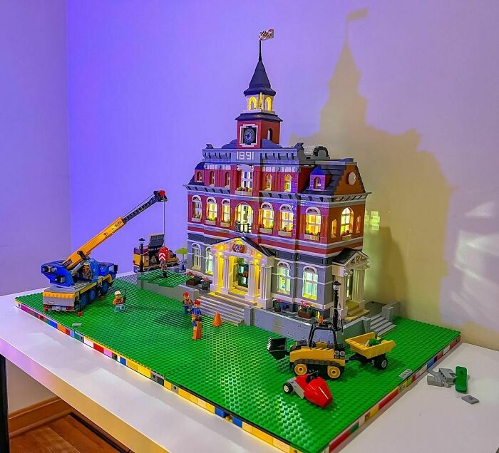 Intricate LEGO builds showcasing a detailed building with construction vehicles and mini-figures on a green baseplate display.