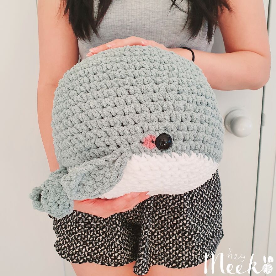 Woman holding a handmade crochet whale with a cute expression, showcasing a creative side hustle.