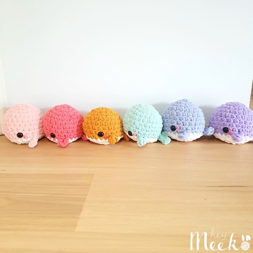 Cute crochet whales in pastel colors lined up on a wooden floor.