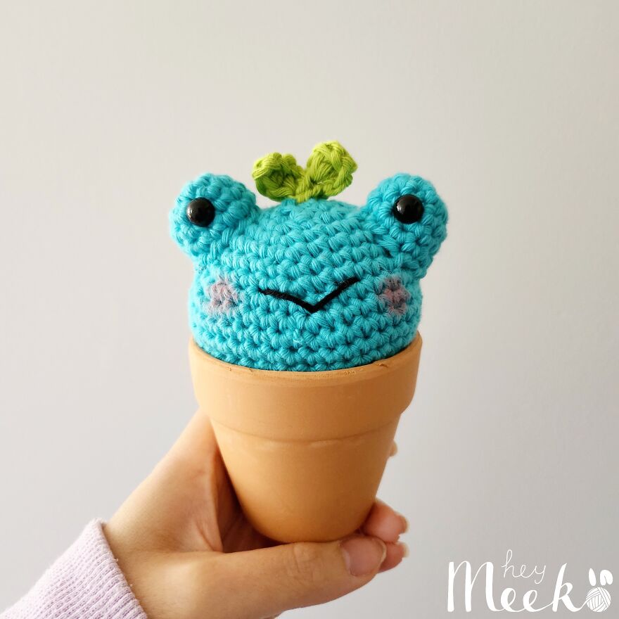 Crocheted blue frog in a clay pot held by a hand, showcasing cute crochet creations.