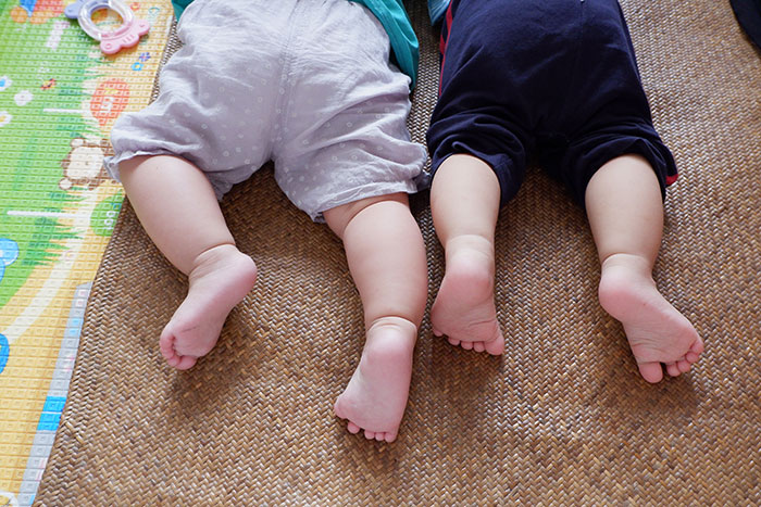 Twin toddlers lying on a mat, wearing different colored pants, focusing on their legs and feet, related to 'medical tattoo'.