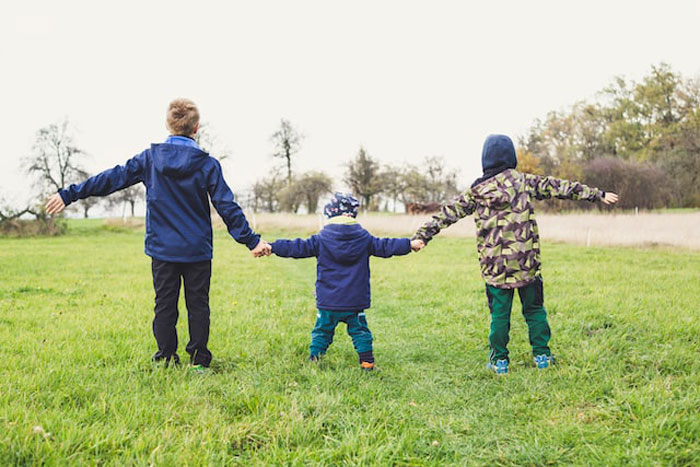Three children holding hands outdoors in a field, illustrating teamwork and avoiding dumbest and most expensive mistakes.