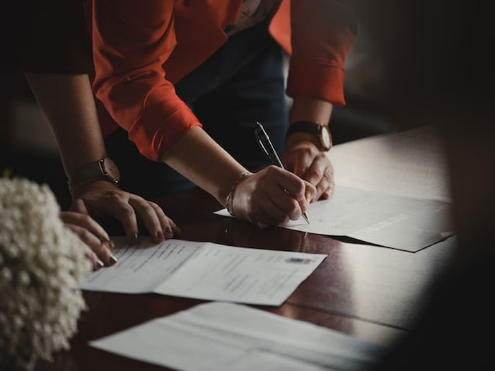 Person in an orange shirt signing documents on a dark desk illustrating dumbest and most expensive mistakes concept.