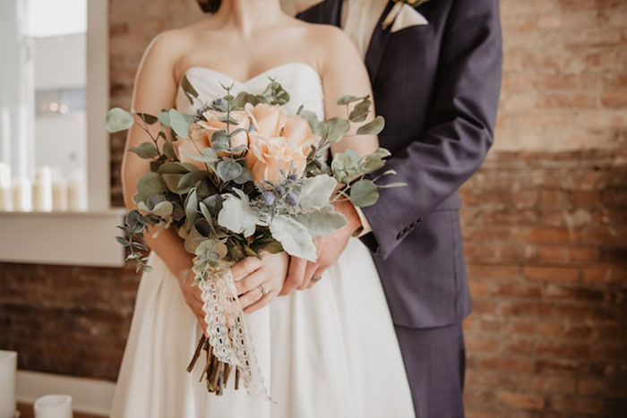 Bride and groom holding a wedding bouquet indoors, illustrating one of the most expensive mistakes seen by others.
