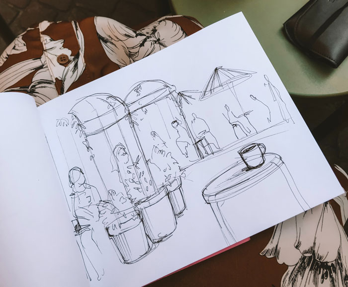 Drawing prompts sketch of a café scene with tables, chairs, and a cup on a table.
