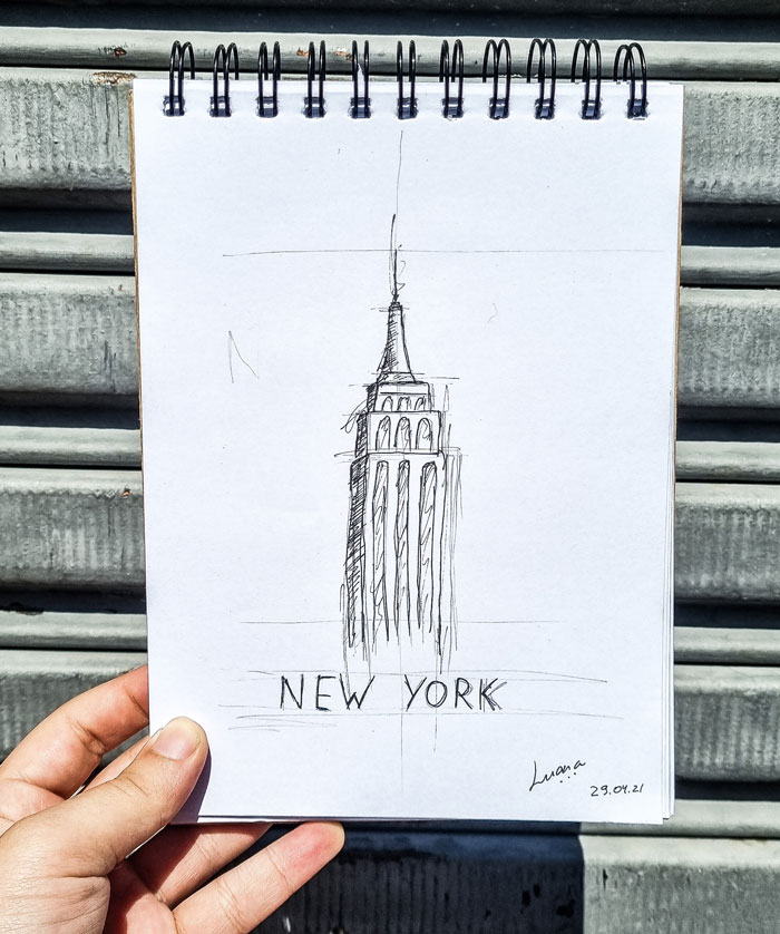 Sketch of a New York building on a notepad held against a metal surface, illustrating drawing prompts for inspiration.