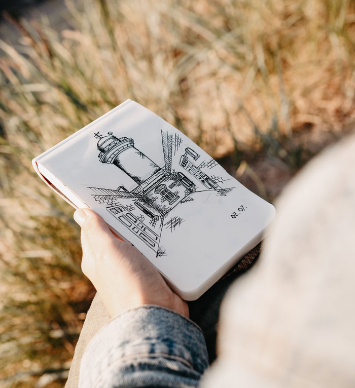 Sketchbook in hand with lighthouse drawing, perfect for when you need drawing prompts and are out of ideas.